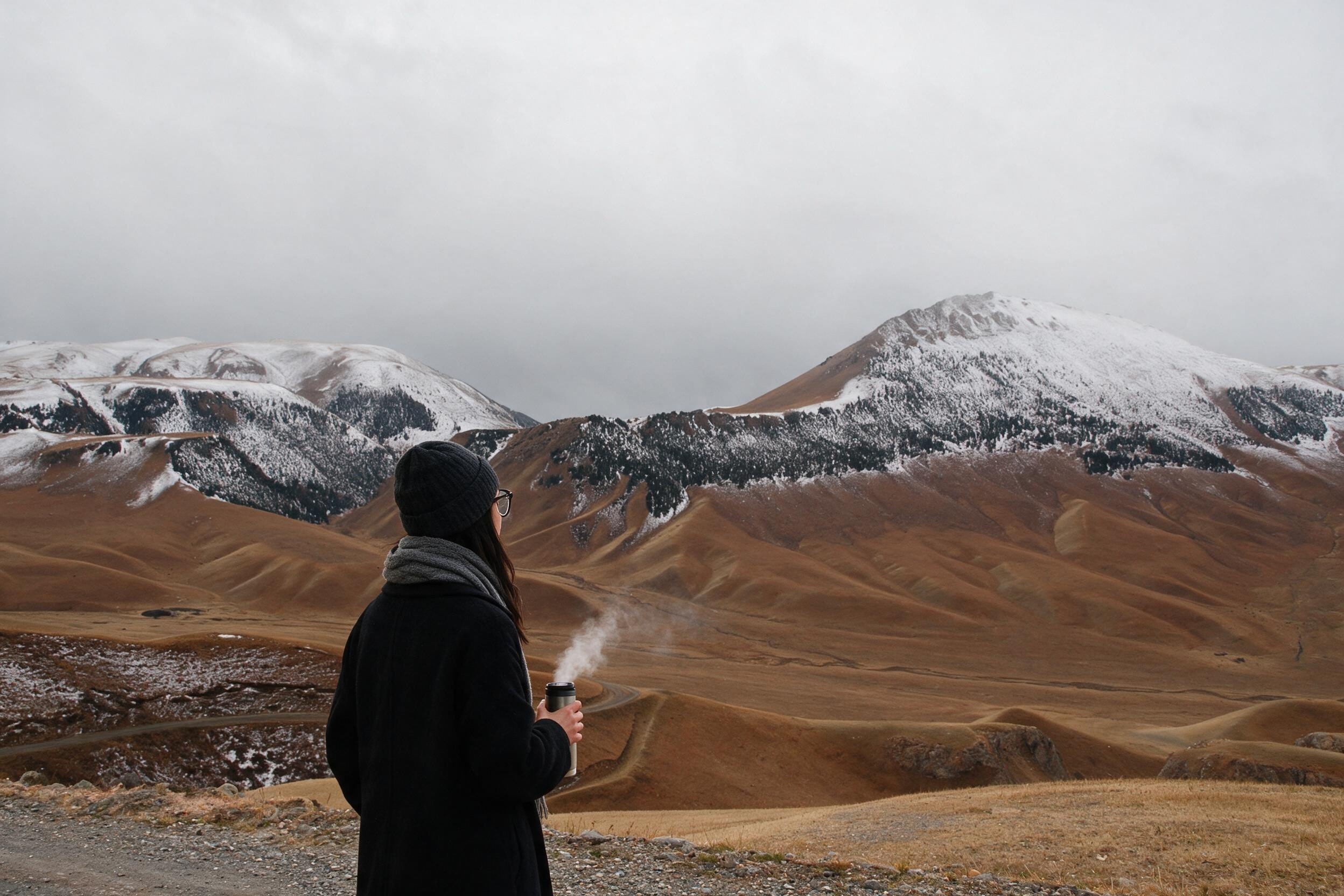 Me at a gravel road edge with a steaming thermos. Fresh snow on the ridges.