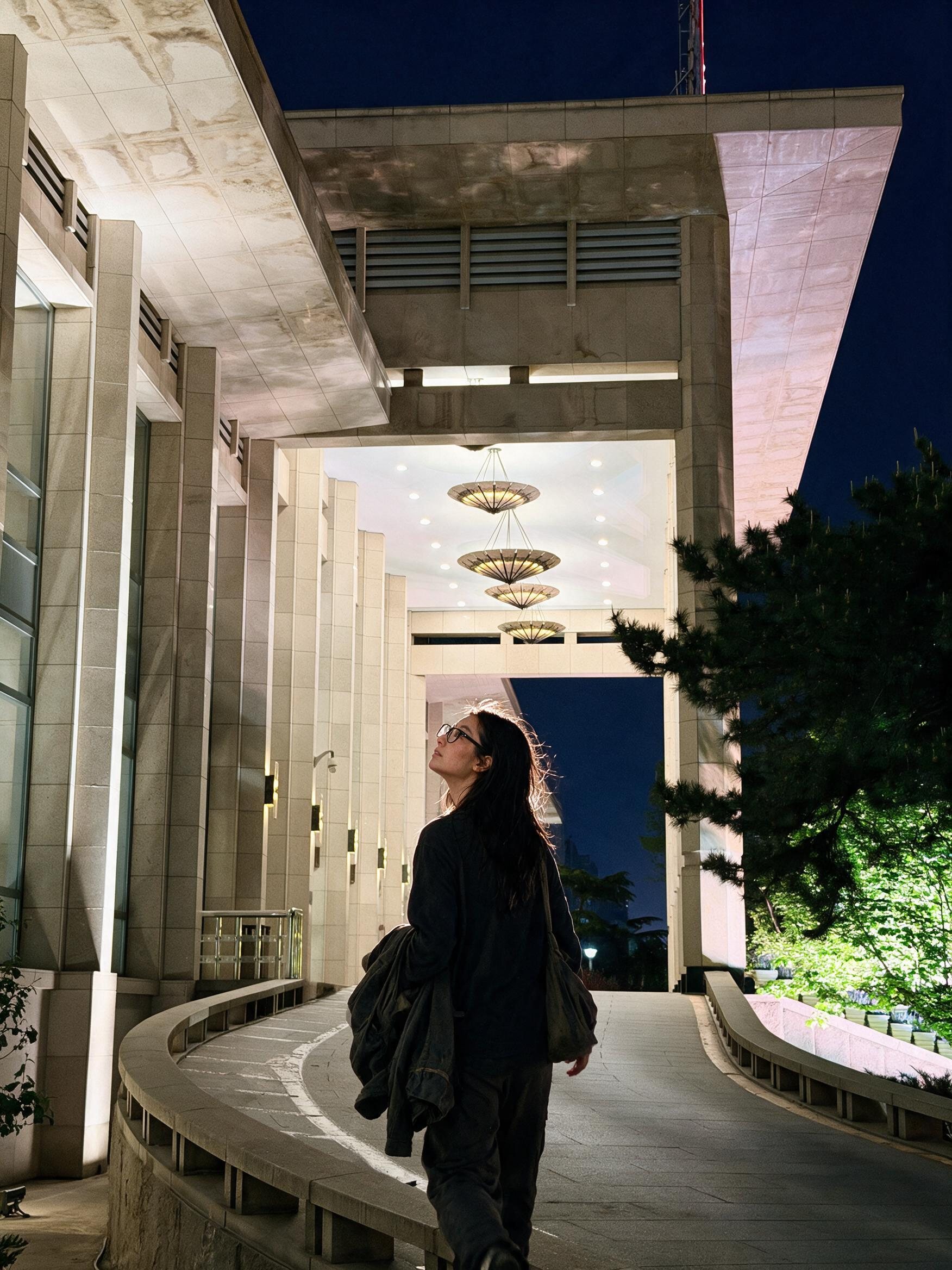 Me walking under the umbrella-shaped lamps on the hotel's curved night drive, floodlit pines beside.