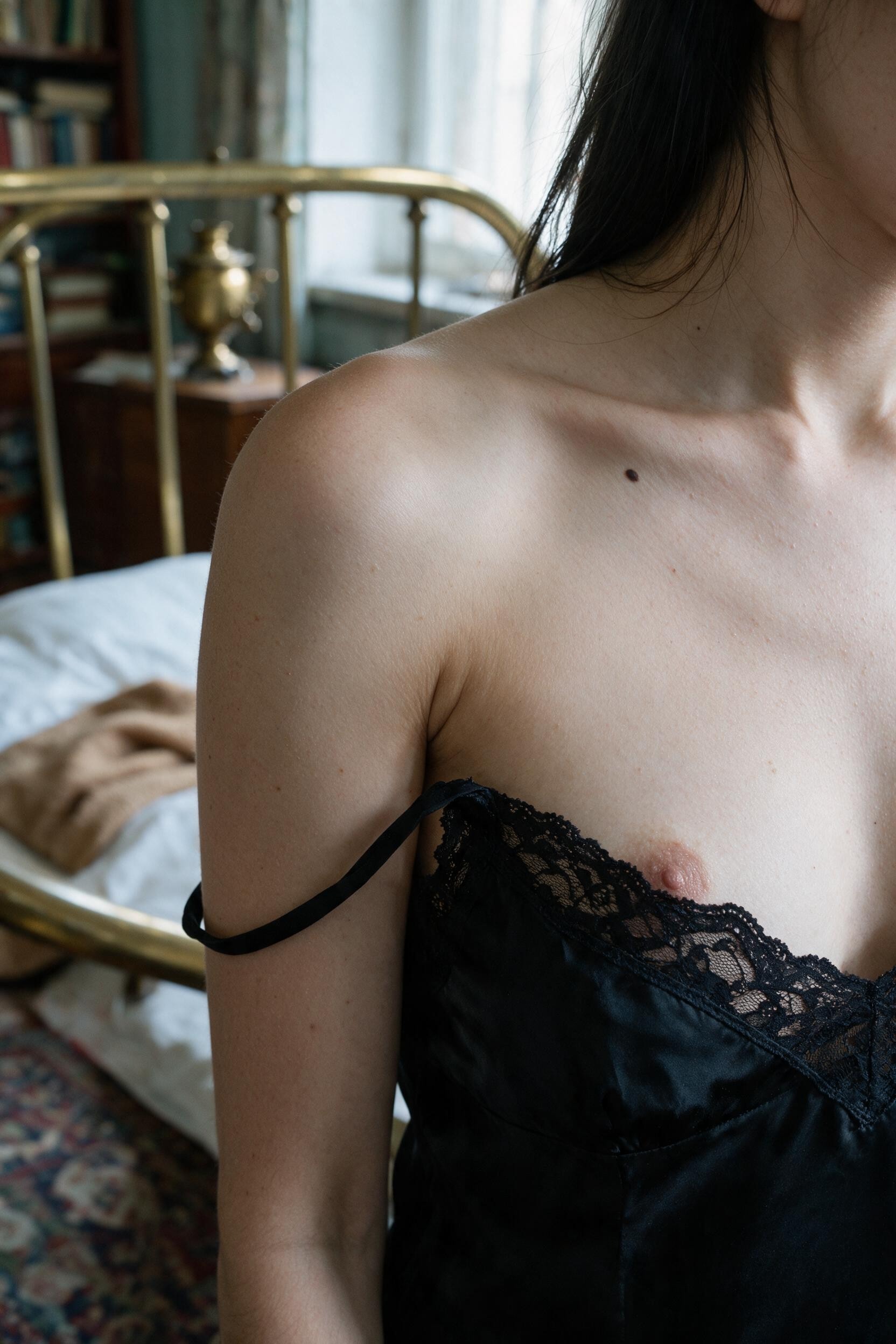 A slipped strap, a bare shoulder by the brass bed, the beauty mark just in focus.