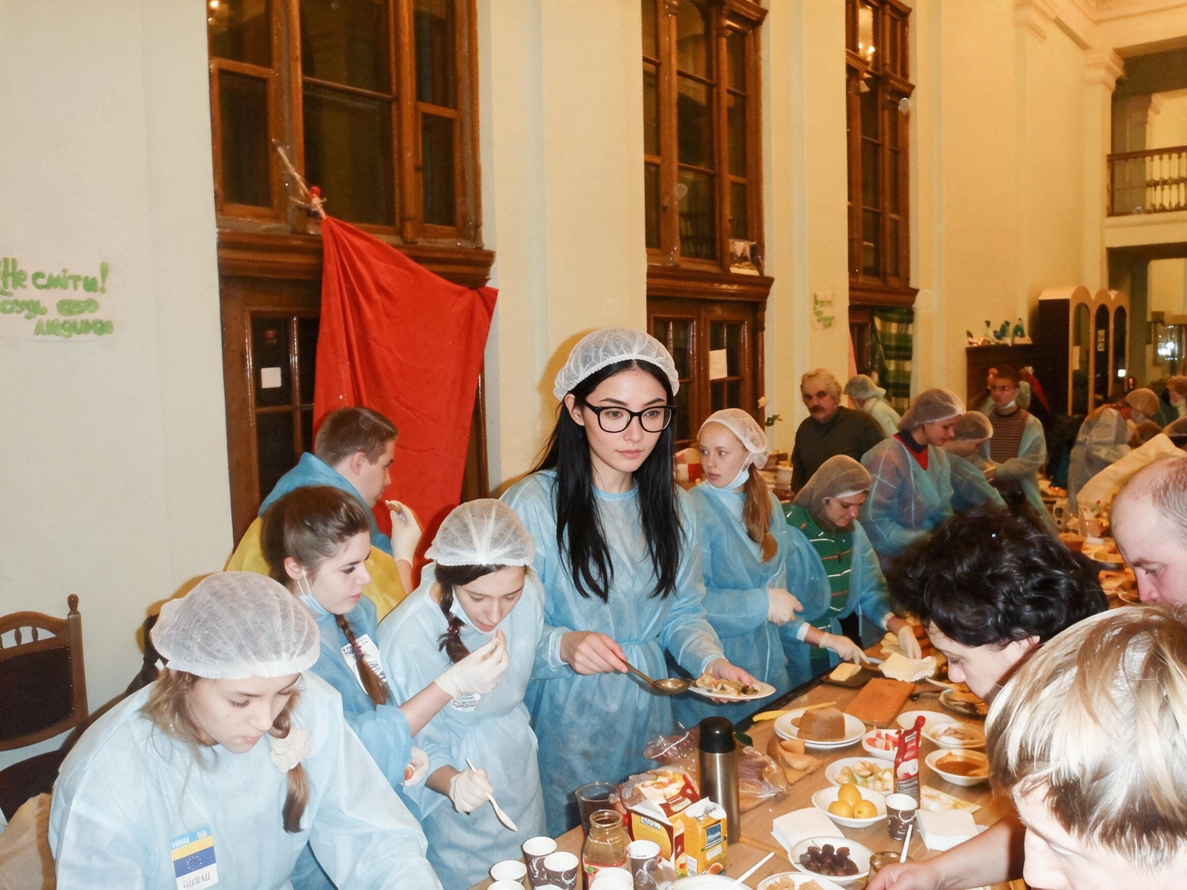 Me in a blue disposable gown ladling food with volunteers at long tables.