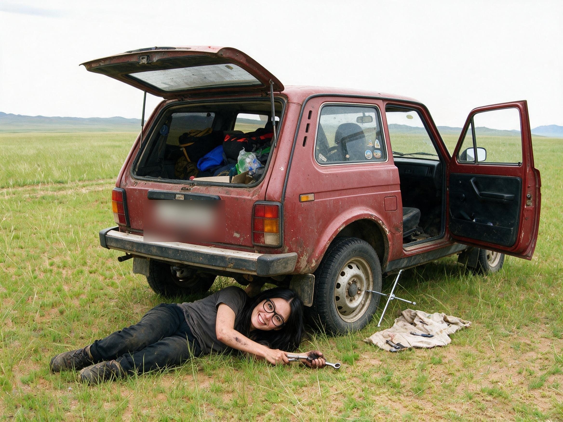Me half under the red Niva on steppe grass, wrench in hand.