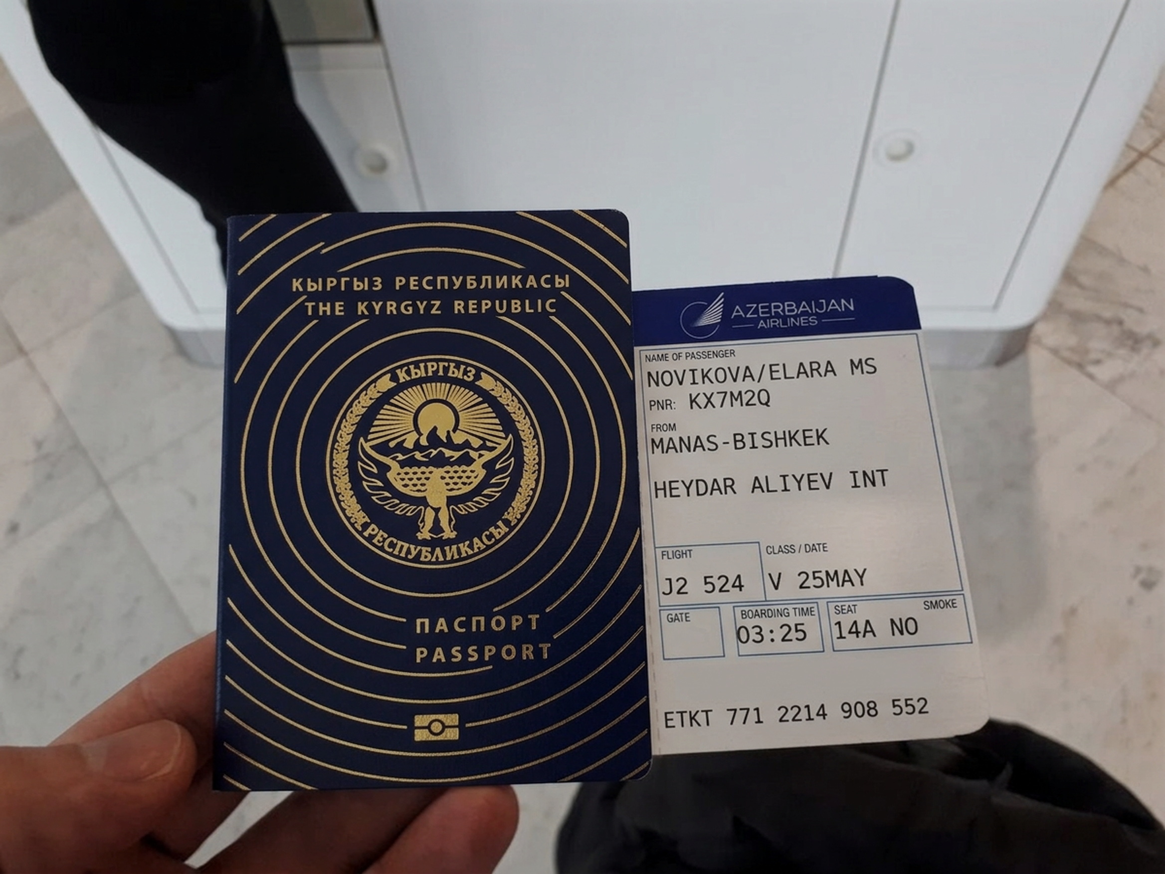 My passport with the boarding pass tucked into it, held over the tiled floor at Manas.