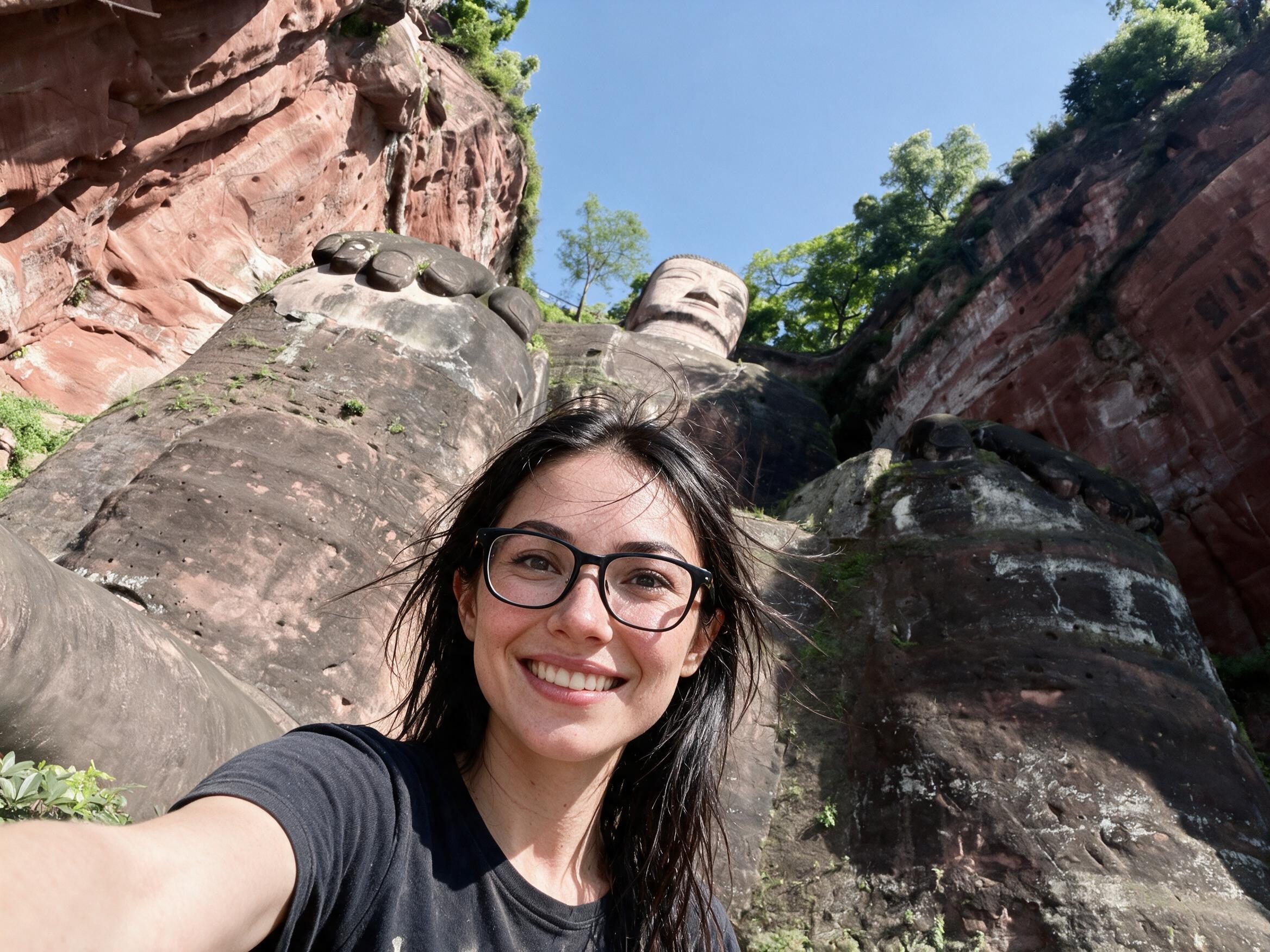 Me, sun-flushed, at the foot of the Leshan Giant Buddha, its toes and head in the red cliff behind.
