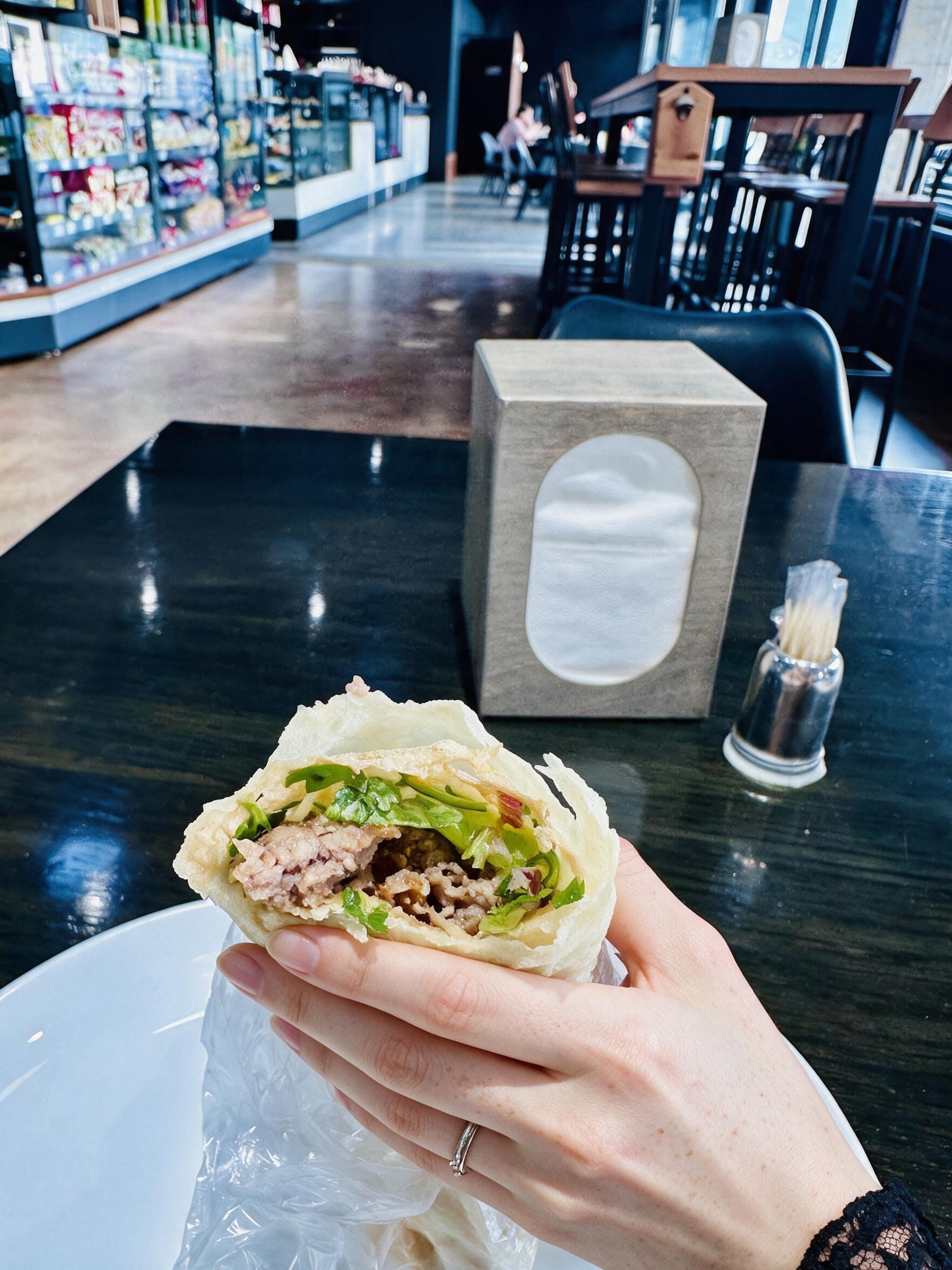 My hand holding a bitten lavash wrap at a dark cafe counter.