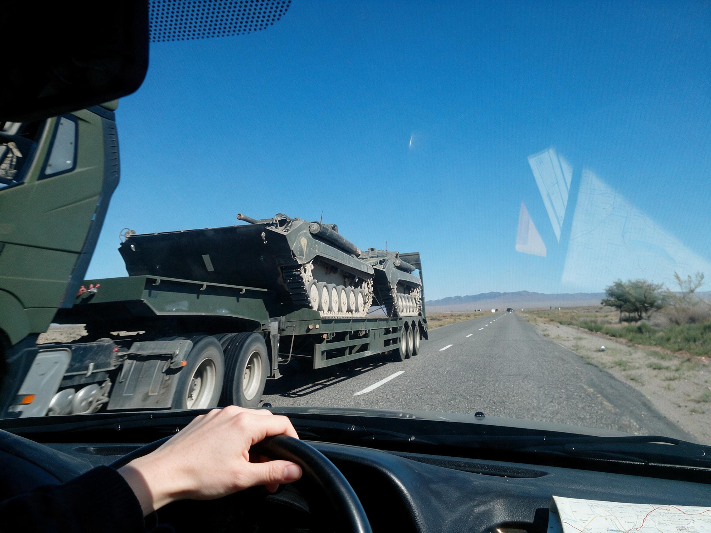 Through the Lada windshield: map on the dash, a truck ahead carrying two tanks.