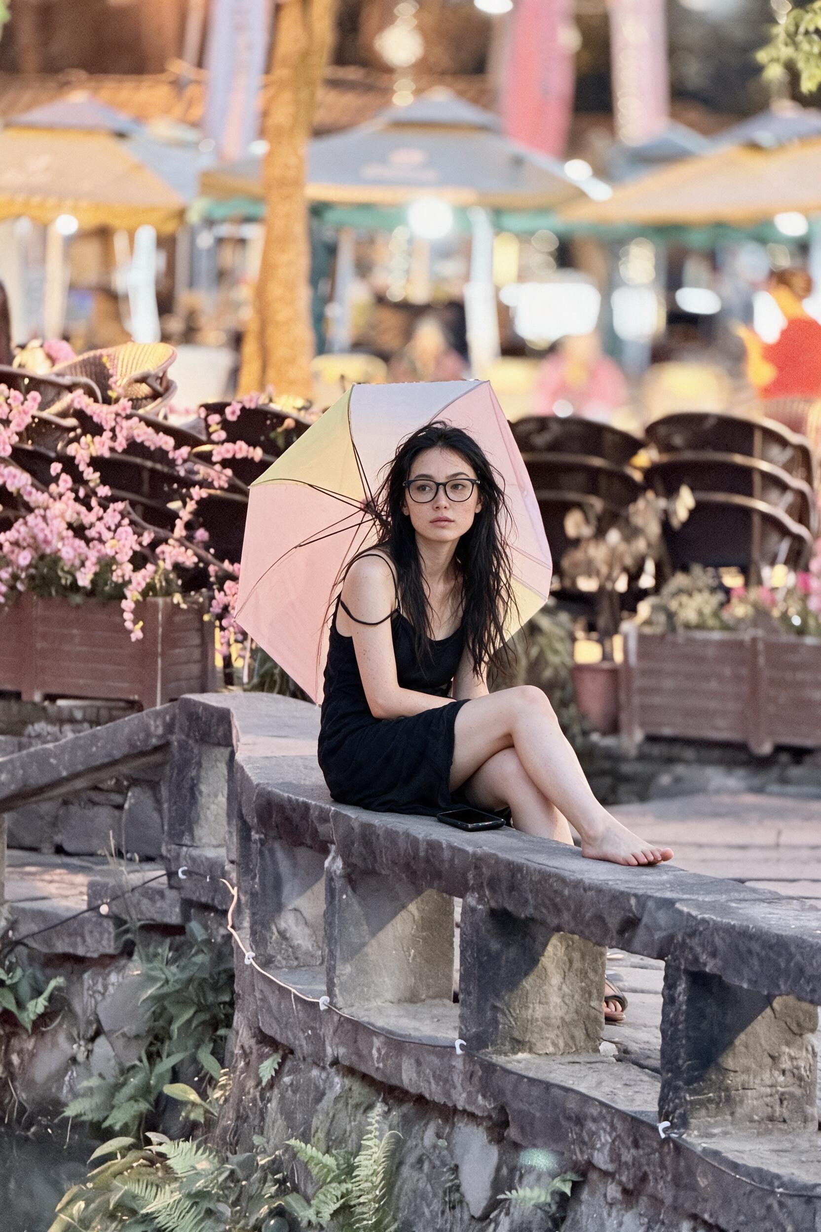 Me in a black summer dress, slipped strap, on a stone bridge parapet under a pastel umbrella.